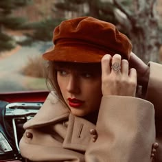 a woman wearing a brown hat is sitting in a car and has her hand on the steering wheel