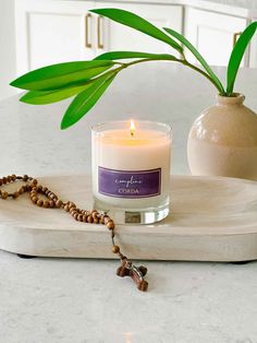 a candle on a marble tray with a beaded necklace and a potted plant in the background