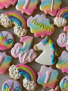 decorated cookies with unicorns and rainbow colors are arranged on a wooden surface for a first birthday party