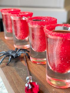 four glasses with red liquid in them sitting on a table next to a black spider