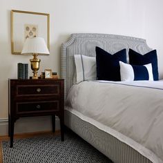 a white bed with blue and white pillows on top of it next to a night stand