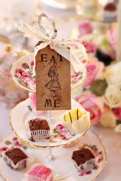 there is a tea party with cupcakes and cakes on the plate, as well as a tag that says eat me