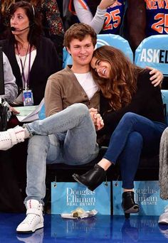 two people sitting next to each other on a bench at a basketball game with fans in the background