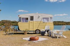 a yellow and white trailer parked on top of a grass covered field next to a lake