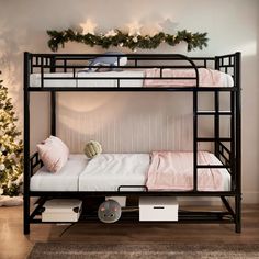 a bunk bed with pink and white sheets on it in front of a christmas tree