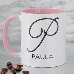 a pink and white coffee mug with the word paula on it next to some coffee beans