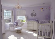 a baby's room with purple walls, white furniture and a chandelier