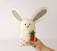 a hand holding up a felt bunny with a carrot in it's mouth,