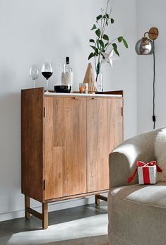 a wooden cabinet sitting next to a couch with wine glasses and a potted plant