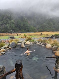 a person in a body of water surrounded by rocks and trees with fog rolling in the background