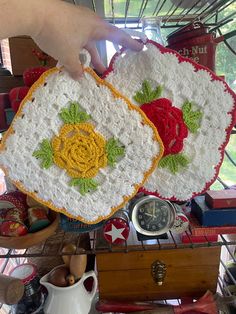 two crocheted coasters with roses on them are sitting on a table next to other items