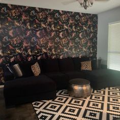 a living room with black couches and colorful wallpaper