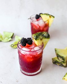 two glasses filled with fruit and garnish next to slices of pineapple