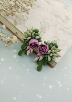 two purple flowers sitting on top of a book next to some white and green leaves