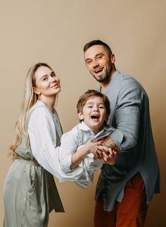 a man and woman holding a young boy in their arms while he laughs at the camera