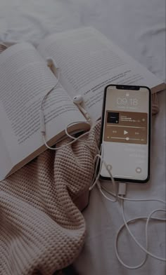 an open book, headphones and cell phone on a bed