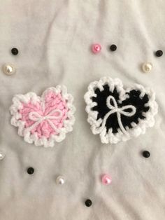 two crocheted hearts sitting on top of a white blanket next to pearls and beads