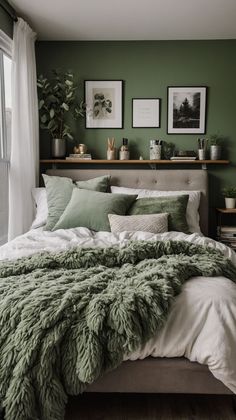 a bed with green blankets and pillows in a bedroom next to a window, plants and pictures on the wall