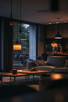 a living room filled with furniture next to a large glass window at night and lit up by hanging lights