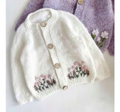 two knitted sweaters with flowers on them, one in white and the other in purple