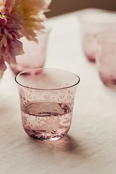 a glass with water and pink flowers in it on a white tablecloth next to other glasses