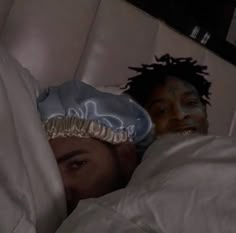 two people laying in bed with white sheets and blankets on their heads, one person has his head wrapped around the other