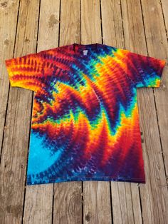 a colorful tie - dyed t - shirt laying on a wooden floor with wood planks