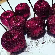 some pink glittered apples sitting on top of a white plate with black pins sticking out of them