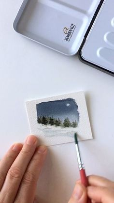 someone is using a brush to paint the landscape on a piece of paper with watercolor pencils