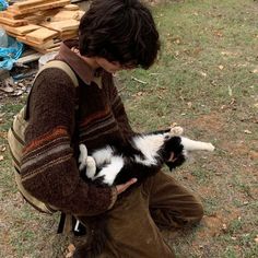 a young man holding a black and white cat in his lap while sitting on the ground