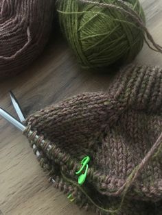 two balls of yarn sitting on top of a wooden floor next to scissors and knitting needles