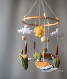 a mobile with birds and clouds hanging from it's sides in front of a gray background