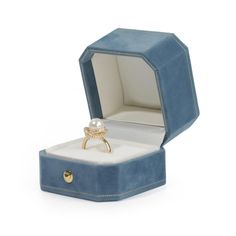 an open blue velvet ring box with a pearl in it