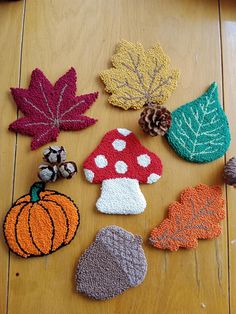 knitted autumn leaves and acorns on a wooden floor with pine cones, pumpkins, and mushrooms