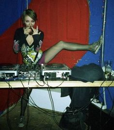 a woman sitting on top of a wooden table next to a red chair and mixing equipment