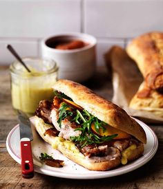 a sandwich with meat and vegetables on a plate next to a cup of mustard sauce