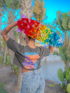 a woman holding a colorful surfboard on her head in front of palm trees and water