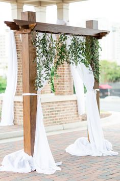 an outdoor wedding ceremony with white draping and greenery on the arbors