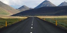 an empty road in the middle of mountains with yellow posts on each side and one lane leading up to it