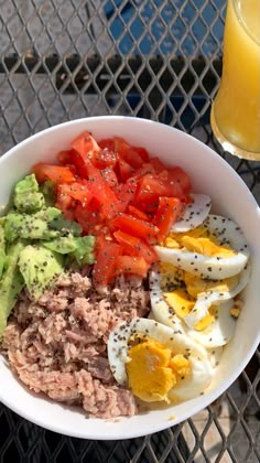 a white bowl filled with meat, eggs and veggies next to a glass of orange juice