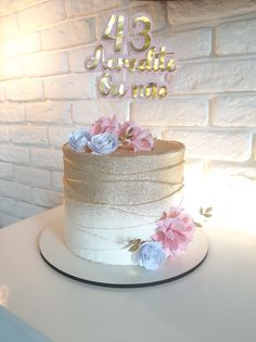 a white cake with pink and blue flowers on top is sitting on a table in front of a brick wall