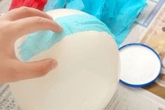 a hand is holding a blue cloth over a white bowl with red and blue tissue paper on it