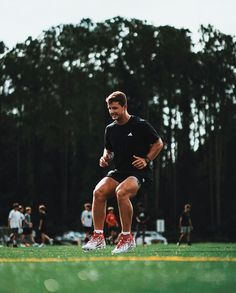 a man is running on the field with other people in the background and trees behind him