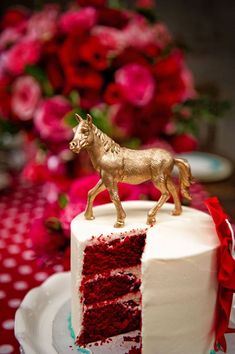 a white cake with red frosting and a golden horse on top, sitting on a plate