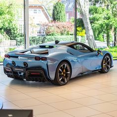 a blue sports car is parked in a showroom with large windows and lots of greenery