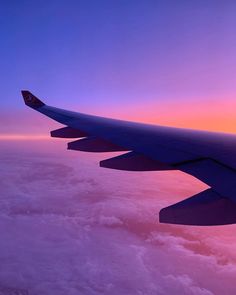 the wing of an airplane as it flies above the clouds at sunset or dawn with pink and purple hues