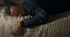 a man laying on top of a bed with his head down and eyes closed while holding onto the pillow