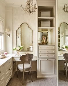 a white bathroom with two chairs and a chandelier above the sink, in front of a large mirror