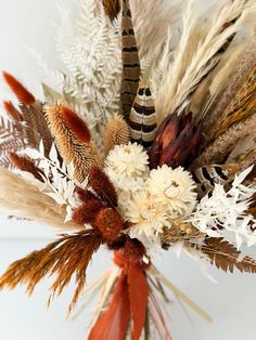 an arrangement of dried flowers and feathers in a vase