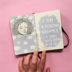 a hand is holding an open notebook with a drawing on it and the words i am floating